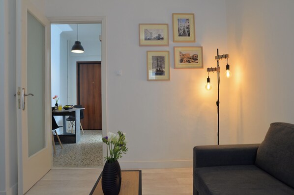 A living room with a sofa, a dining area with a table and chairs, and a hallway leading to another room. - Alter Ego Apartments (Athens)