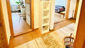 Un vaste espace de vie agrémenté d’un grand tapis, d’une étagère blanche et d’un luminaire suspendu.