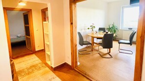 Un intérieur moderne avec un plancher en bois, un tapis à motifs, un coin repas comprenant deux chaises et une table, et un grand miroir qui reflète la pièce.