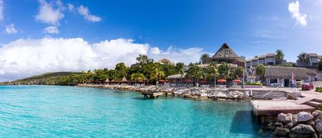 Ein Resort mit Pool, Strand und strohgedeckten Gebäuden.