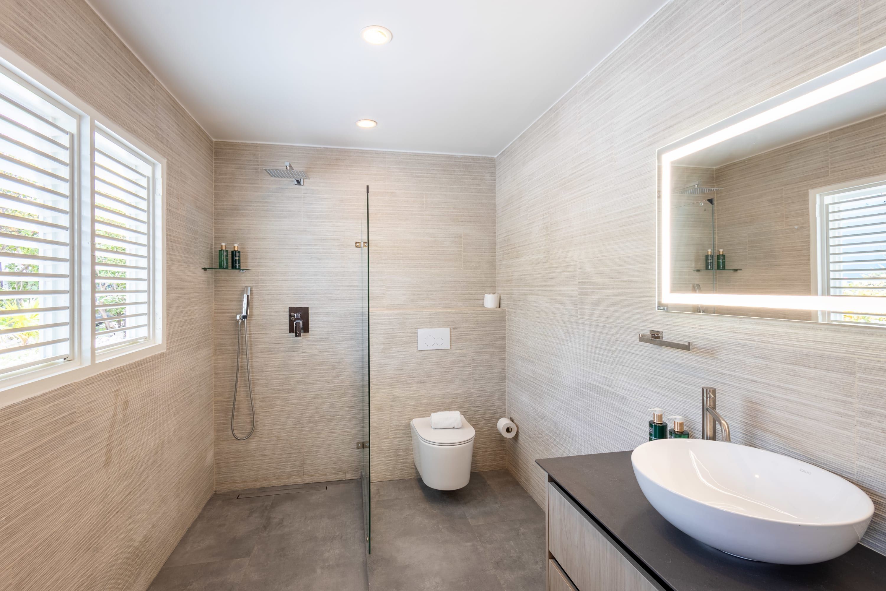 Un baño moderno con un lavamanos blanco grande, una cabina de ducha de vidrio y un espejo amplio.