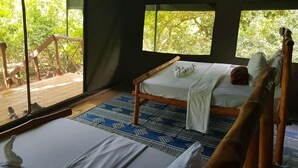 A room with a bed, a wooden chair, and a view of the outdoors. - Camp Seluu (Mloka)