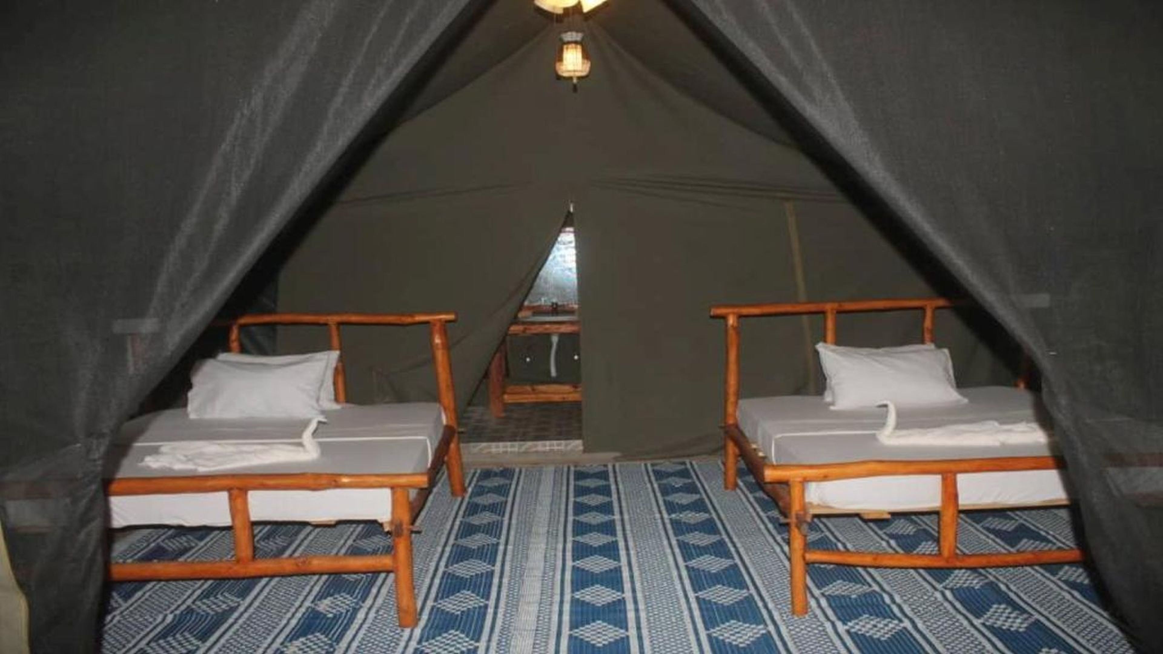 A tent with two wooden beds, a patterned floor, and a central light fixture.