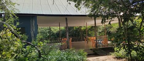 Un espacio al aire libre techado con lámina metálica, rodeado de abundante vegetación y árboles.