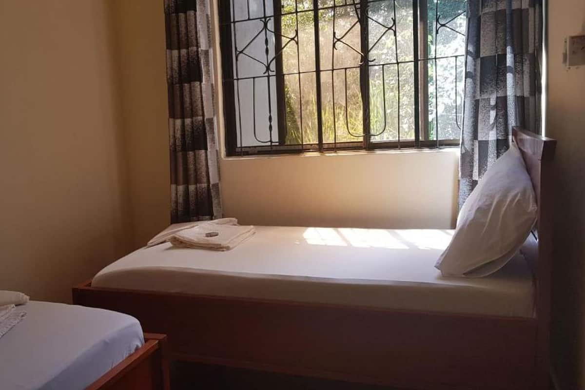 Una habitación pequeña con cama individual, ventana con barrotes y cortinas.