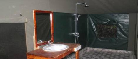 A tent with a wooden chair, a sink, and a shower.