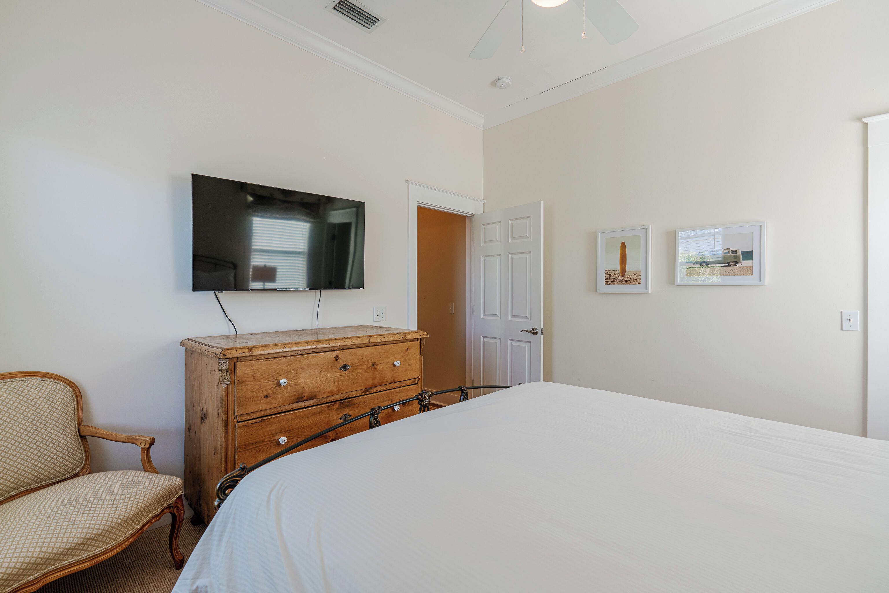 A bedroom with a bed, wooden dresser, chair, and a television mounted on the wall.