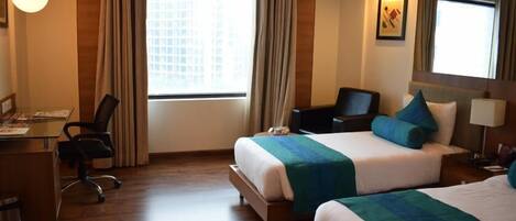A hotel room with two beds, a desk, a chair, a lamp, and a window with curtains.