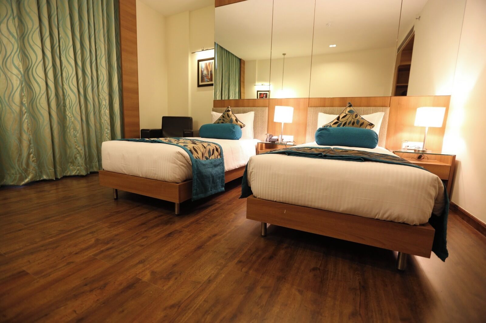 A hotel room with two beds, wooden flooring, and a large mirror above the beds.