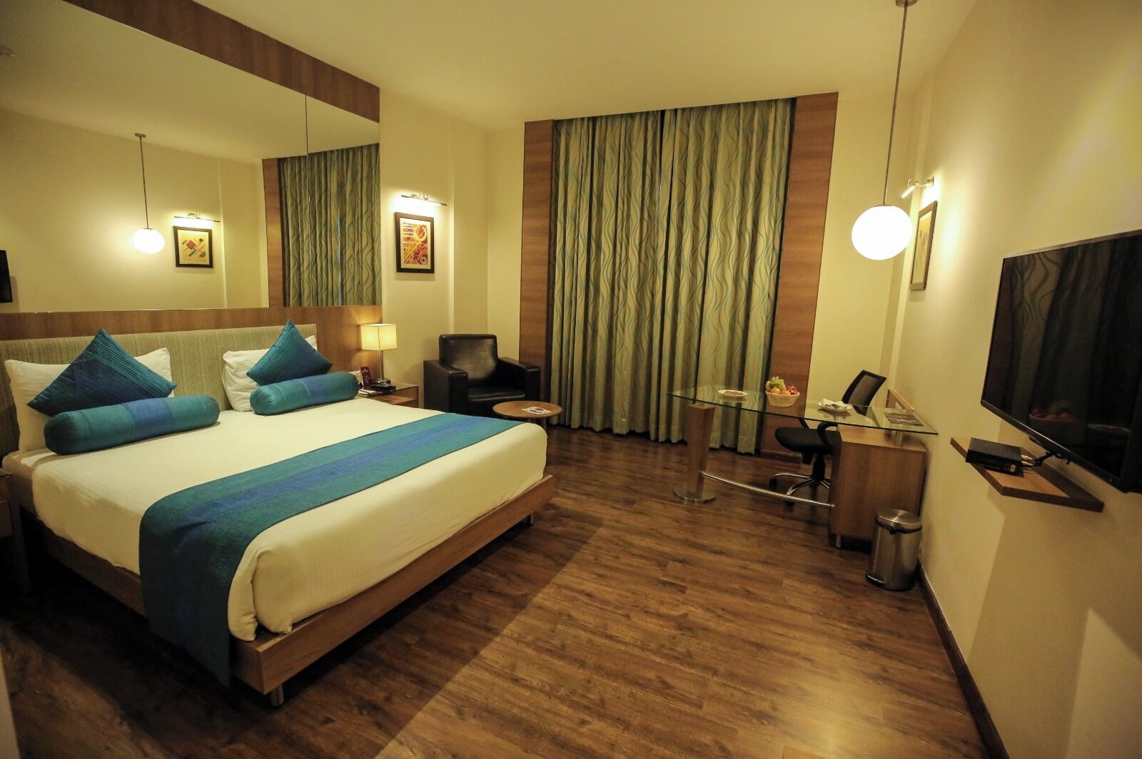 Habitación de hotel con una cama grande, un escritorio con computadora, una silla, un televisor y una ventana con cortinas.