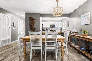 Un coin repas avec une table en bois et des chaises blanches, une cuisine en arrière-plan et un élément décoratif mural.