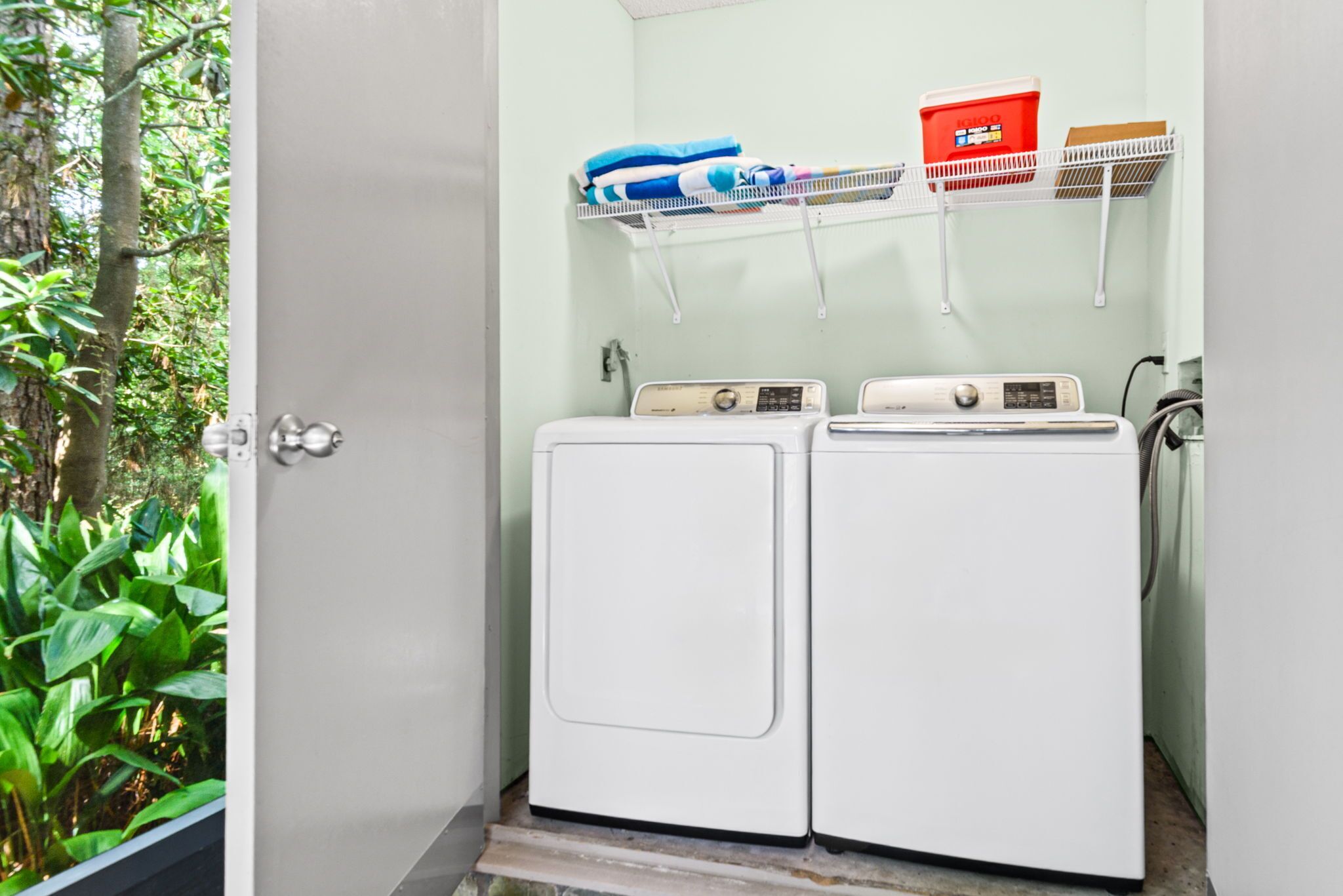 A laundry room with two white washing machines, a shelf with folded clothes, and a red detergent box.