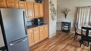 A compact kitchen with wooden cabinets, a refrigerator, a microwave, and a small dining table with chairs. - Charlie’s on the Water - a Charming 3-bedroom house with a lake view-Sabula (Sabula)
