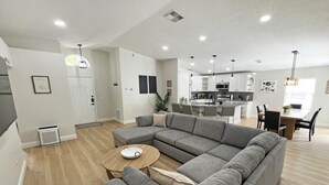 A modern living room with a sectional sofa, a round coffee table, and a dining area with a table and chairs. - Stardust Villa 4 Bedroom Home by RedAwning (Kissimmee)
