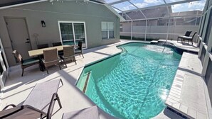 A covered outdoor swimming pool with lounge chairs and a table, surrounded by a covered patio area. - Stardust Villa 4 Bedroom Home by RedAwning (Kissimmee)