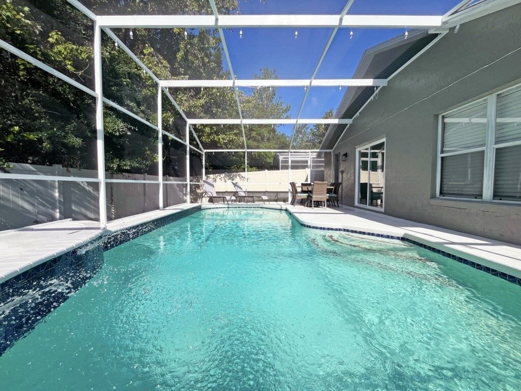 A swimming pool with a covered area, surrounded by a fence, and a building with a window to the right.