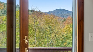 A view from a balcony with a wooden railing, overlooking a forested area with autumn-colored trees and a hill in the distance. - The Getaway 4 Bedroom Home (Pittsfield)