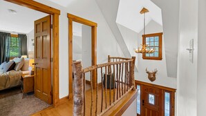 A spacious bedroom with a large bed, a nightstand, and a dresser. There is a wooden staircase with a railing leading to a landing. - The Getaway 4 Bedroom Home (Pittsfield)