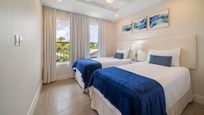 A hotel room with two beds, a balcony with curtains, and artwork on the wall. - Coral Beach 202 2 Bedroom Condo (Speightstown)