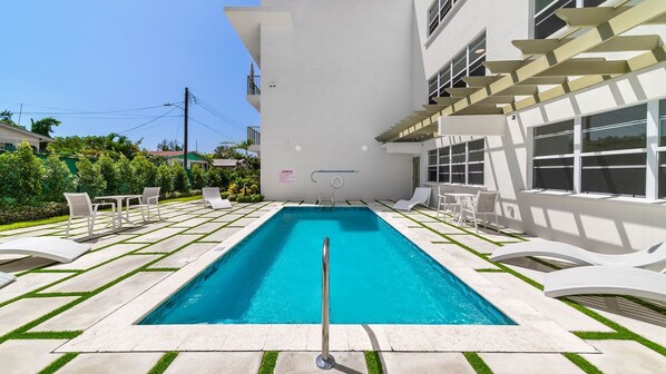 Ein Swimmingpool mit einer Metallleiter, umgeben von weißen Liegestühlen und einer gefliesten Terrasse.