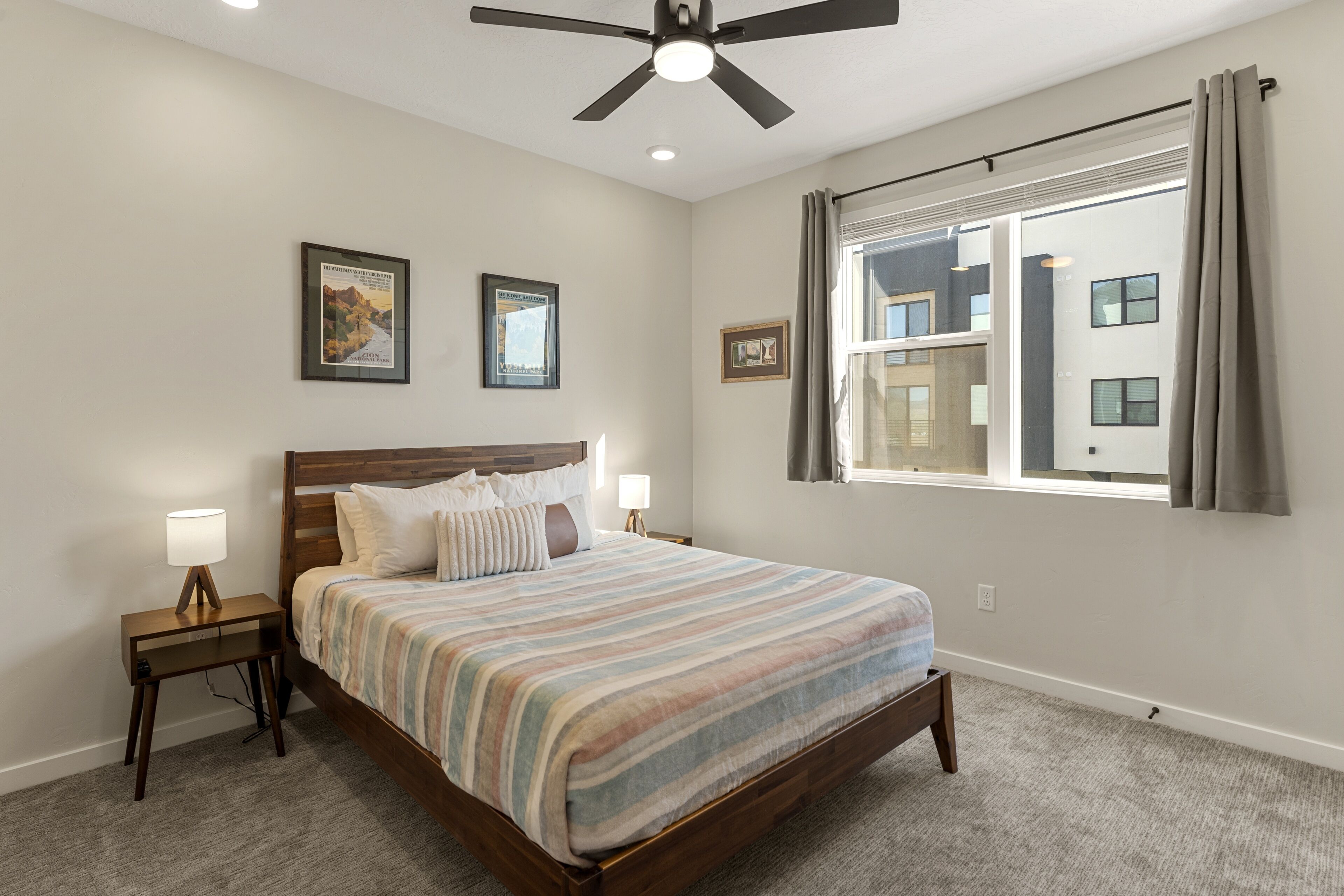 A bedroom with a bed, a nightstand, a ceiling fan, and a window with curtains.