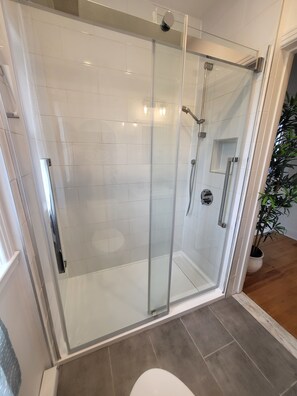 A modern bathroom with a glass-enclosed shower, white tiled walls, and a potted plant.