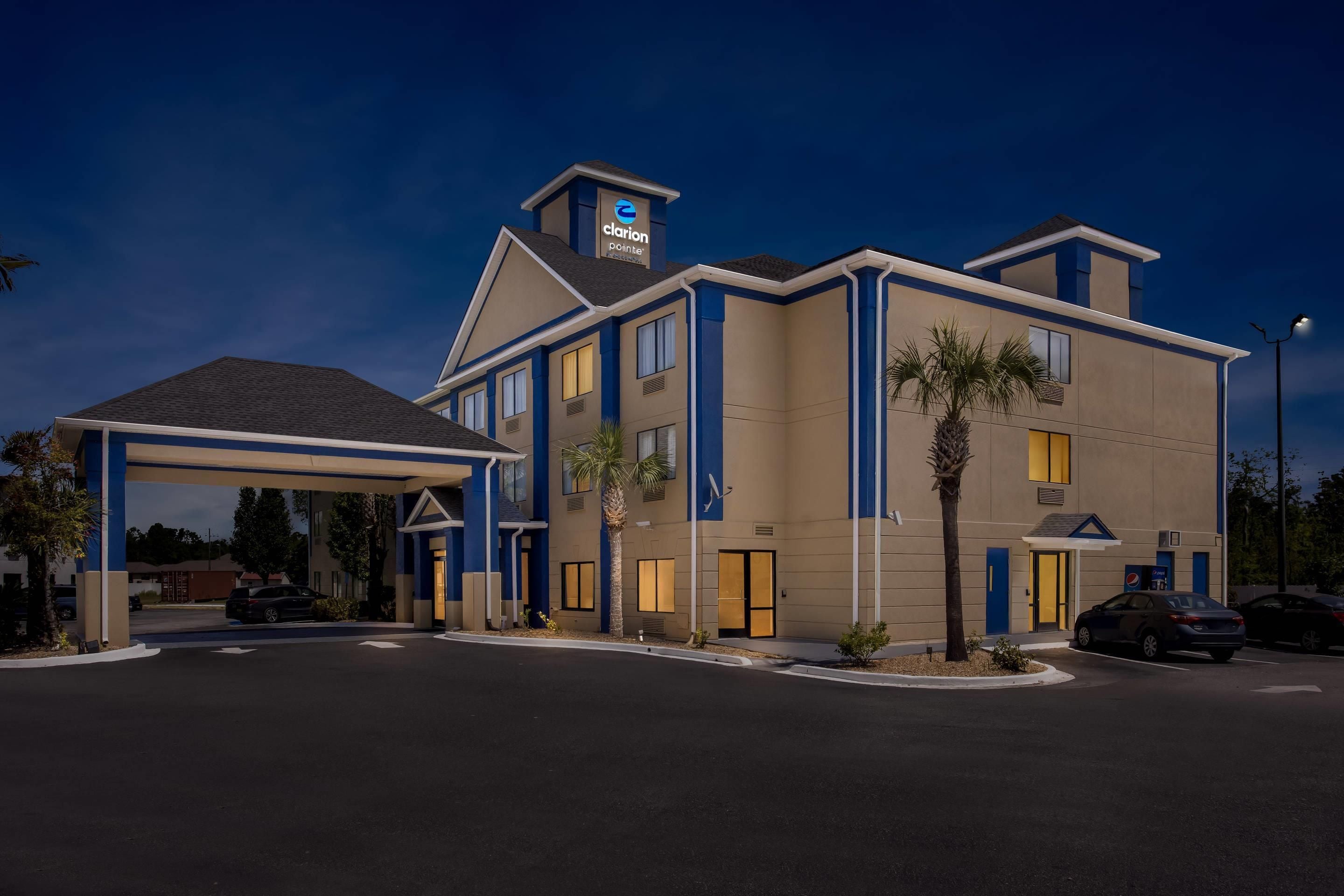Un hotel Clarion Pointe con vestíbulo cubierto, múltiples ventanales y aparcamiento.