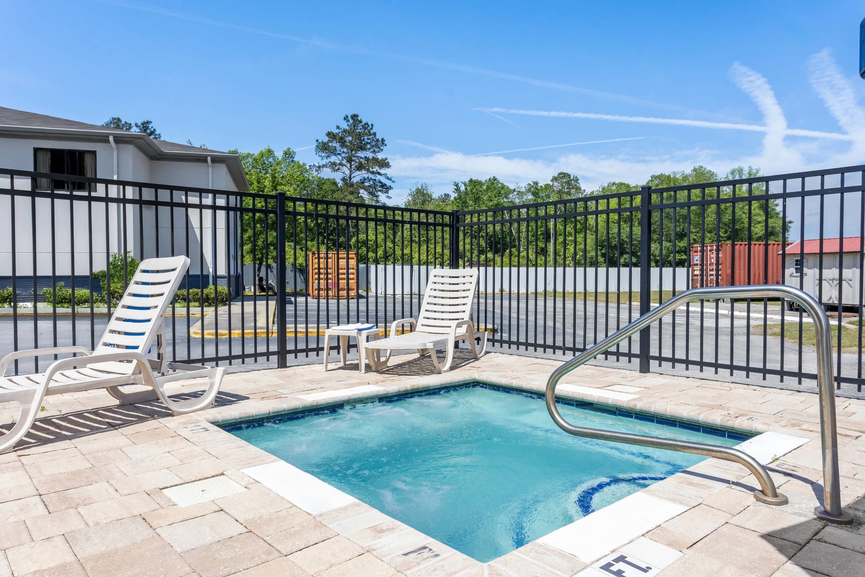 A swimming pool with lounge chairs, a metal fence, and a building in the background.