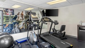 Un gimnasio con cintas de correr, elíptica y un espejo grande.