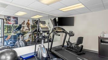 Un gimnasio con cintas de correr, elíptica y un espejo grande.