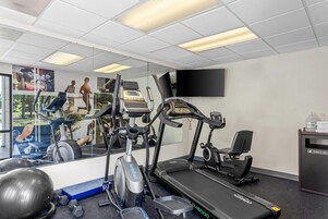 Un gimnasio con cintas de correr, elíptica y un espejo grande.