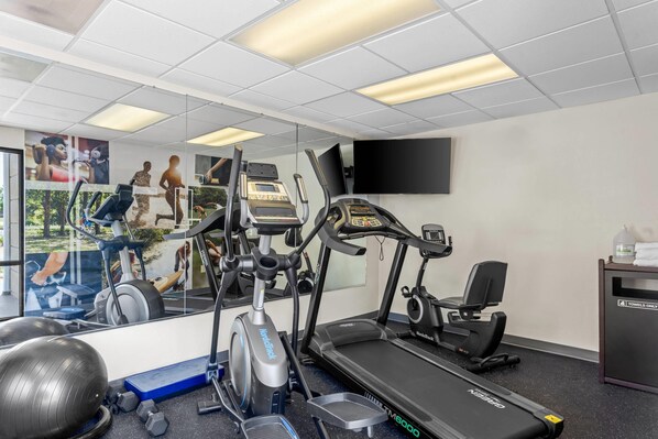Un gimnasio con cintas de correr, elíptica y un espejo grande.