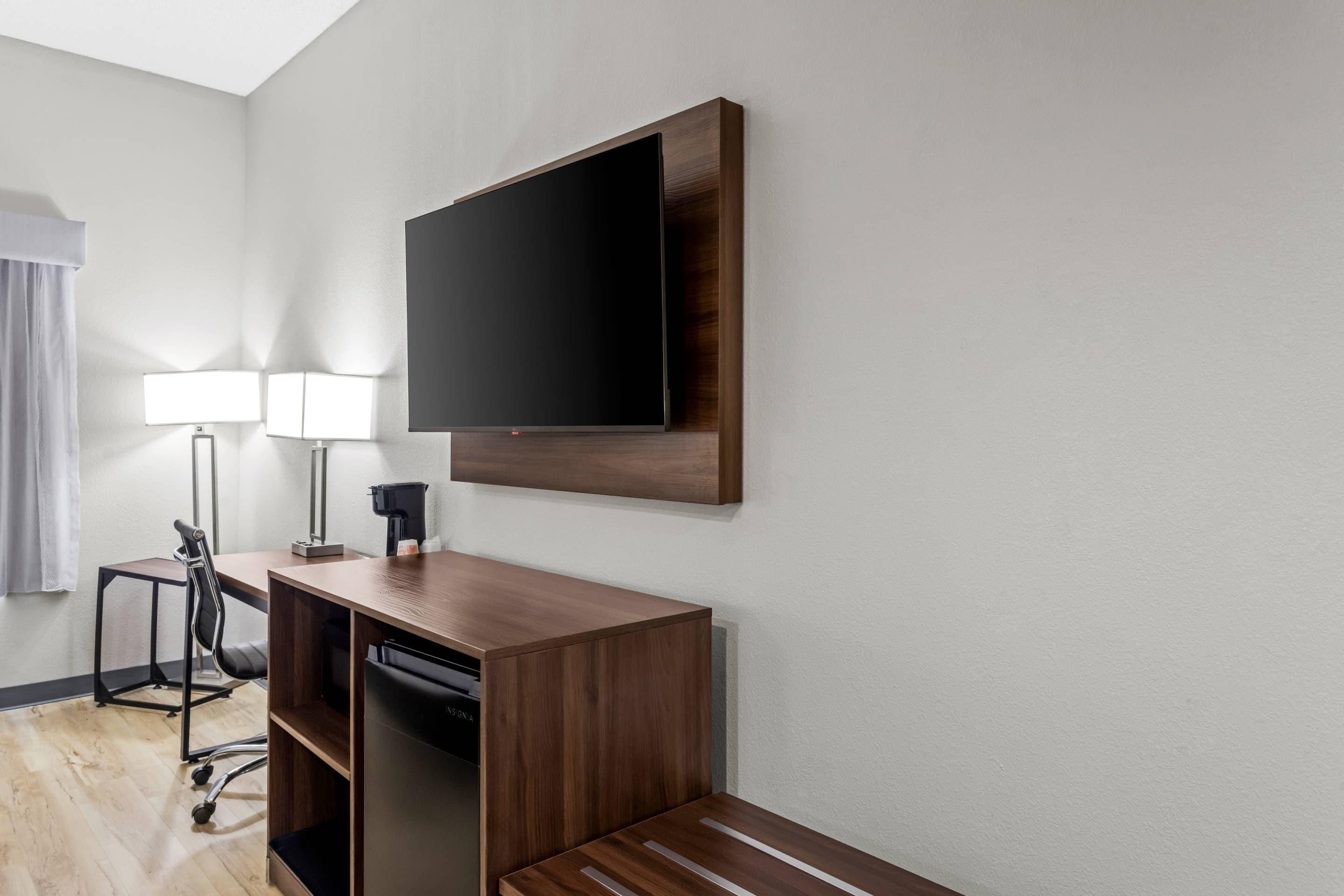 A hotel room with a desk, chair, TV, and lamps.