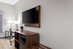 Habitación de hotel con escritorio, silla, televisor y lámparas.