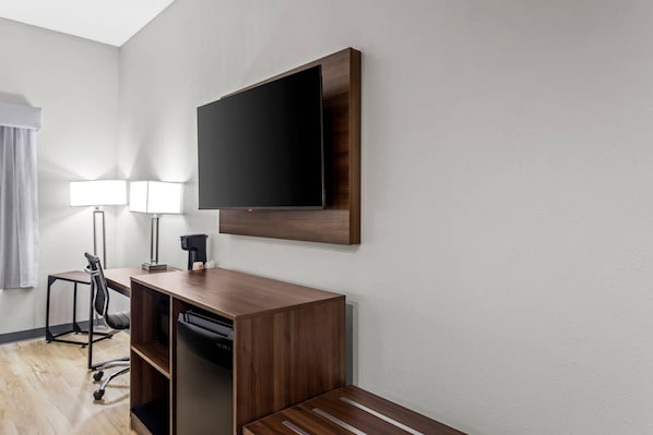 A hotel room with a desk, chair, TV, and lamps.