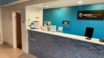 A hotel reception desk with a blue wall, a sign for Clarion Pointe by Choice Hotels, and informational brochures.