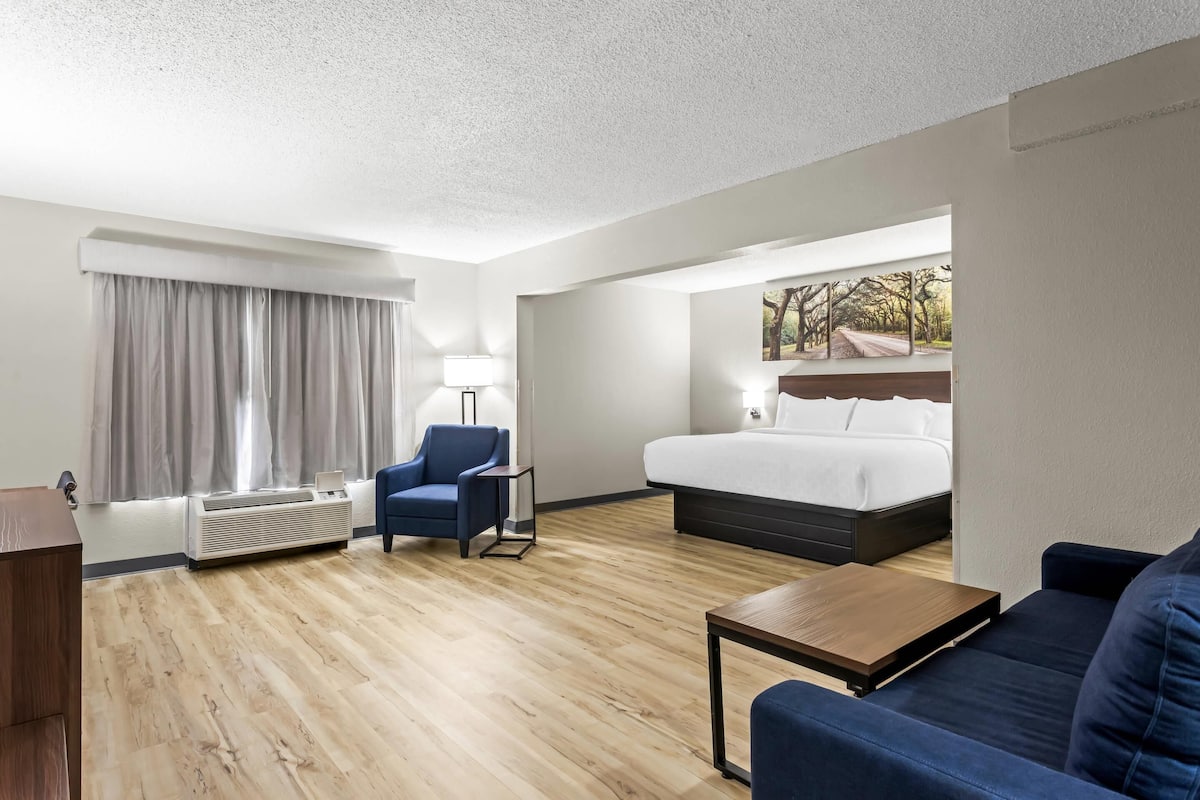 A hotel room with a bed, a desk, a chair, a sofa, and a window with curtains.