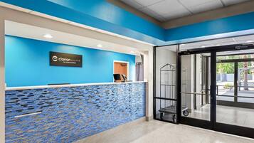 Zona de recepción con una decoración azul y blanca, un mostrador de recepción, una puerta de cristal que da al exterior y un suelo de baldosas.