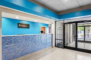 A reception area with a blue and white color scheme, a reception desk, a glass door leading outside, and a tiled floor. - Jesup Inn & Suites (Jesup)