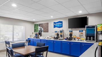 Una cafetería moderna con armarios azules, una mesa de madera y una pantalla de televisión grande.