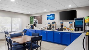 Una cafetería moderna con armarios azules, una mesa de madera y una pantalla de televisión grande.