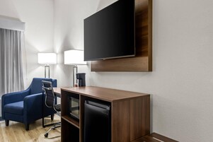 Habitación de hotel con televisión de pantalla plana en la pared, un escritorio con silla, cafetera y lavavajillas.