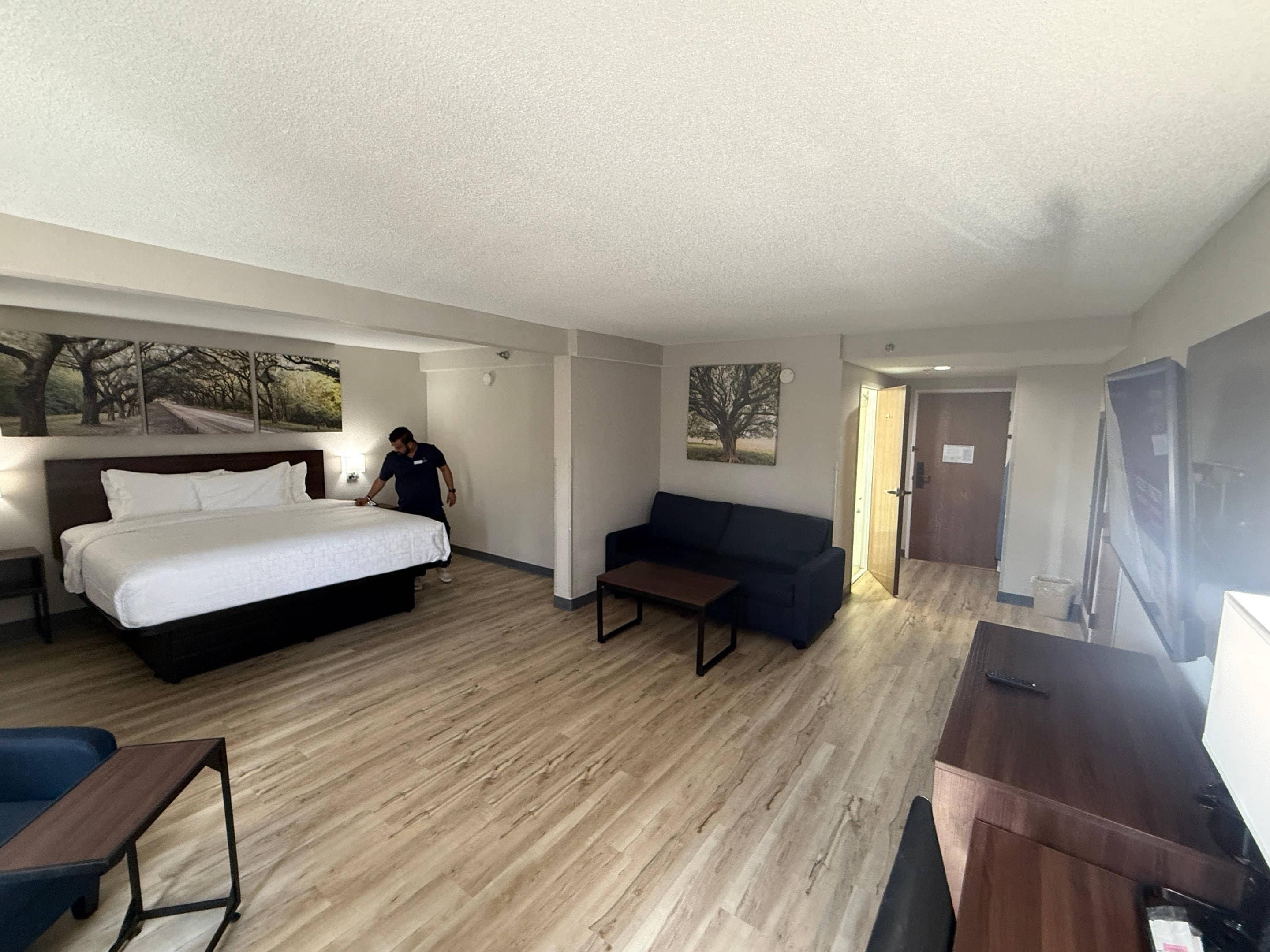 A hotel room with a bed, a sofa, a small table, and a TV.