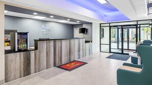 Zona de recepción con mostrador de madera, puerta de cristal y área de descanso con sillas.