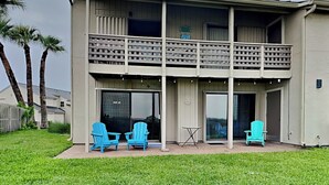 Un bâtiment à deux étages doté d’un balcon, de grandes fenêtres et d’un espace extérieur aménagé avec des chaises.