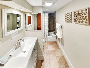 Un baño moderno con una bañera blanca grande, ducha y retrete. Hay dos espejos, un perchero y paneles decorativos en la pared.