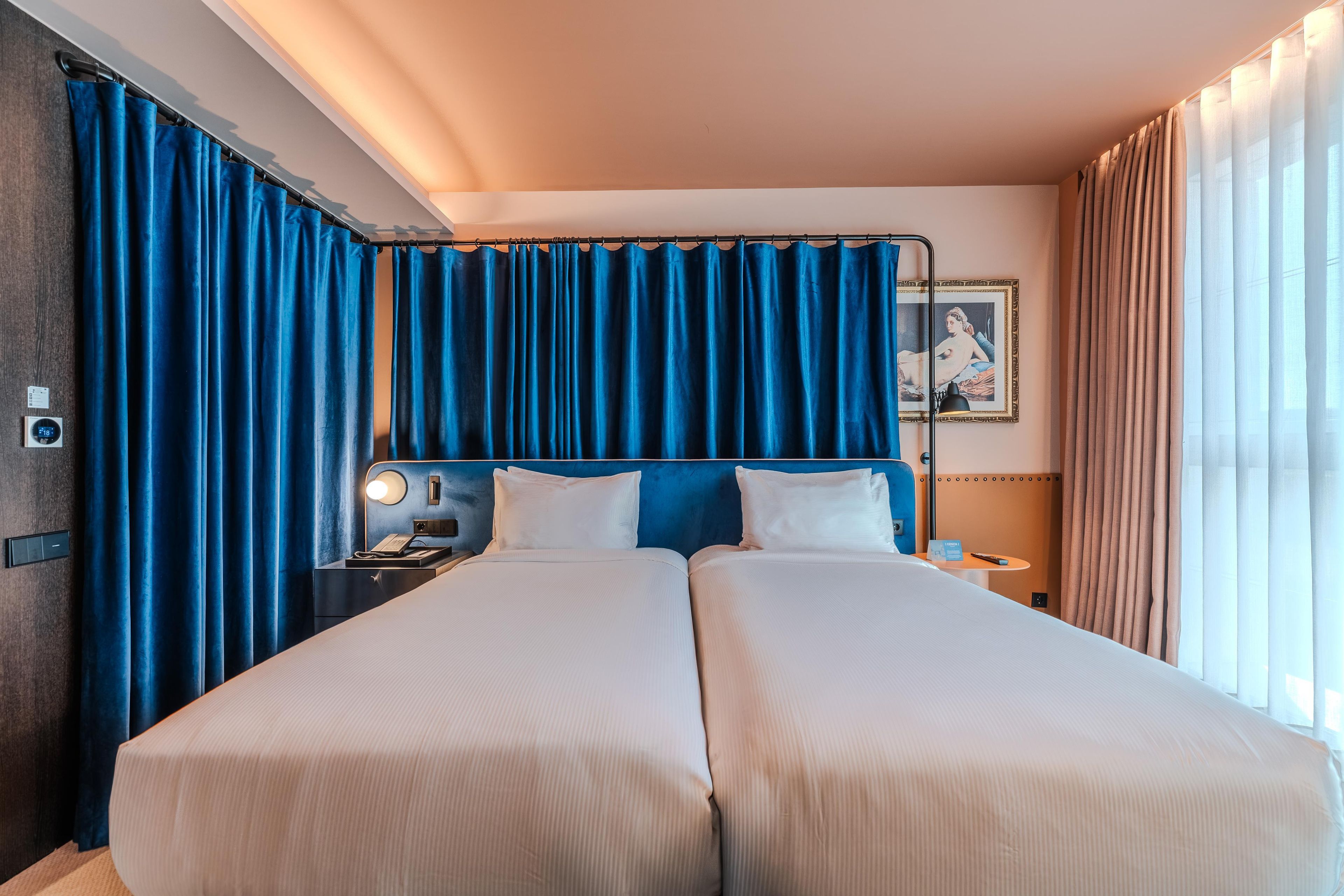 A hotel room with two beds, a nightstand, a lamp, and a painting on the wall.