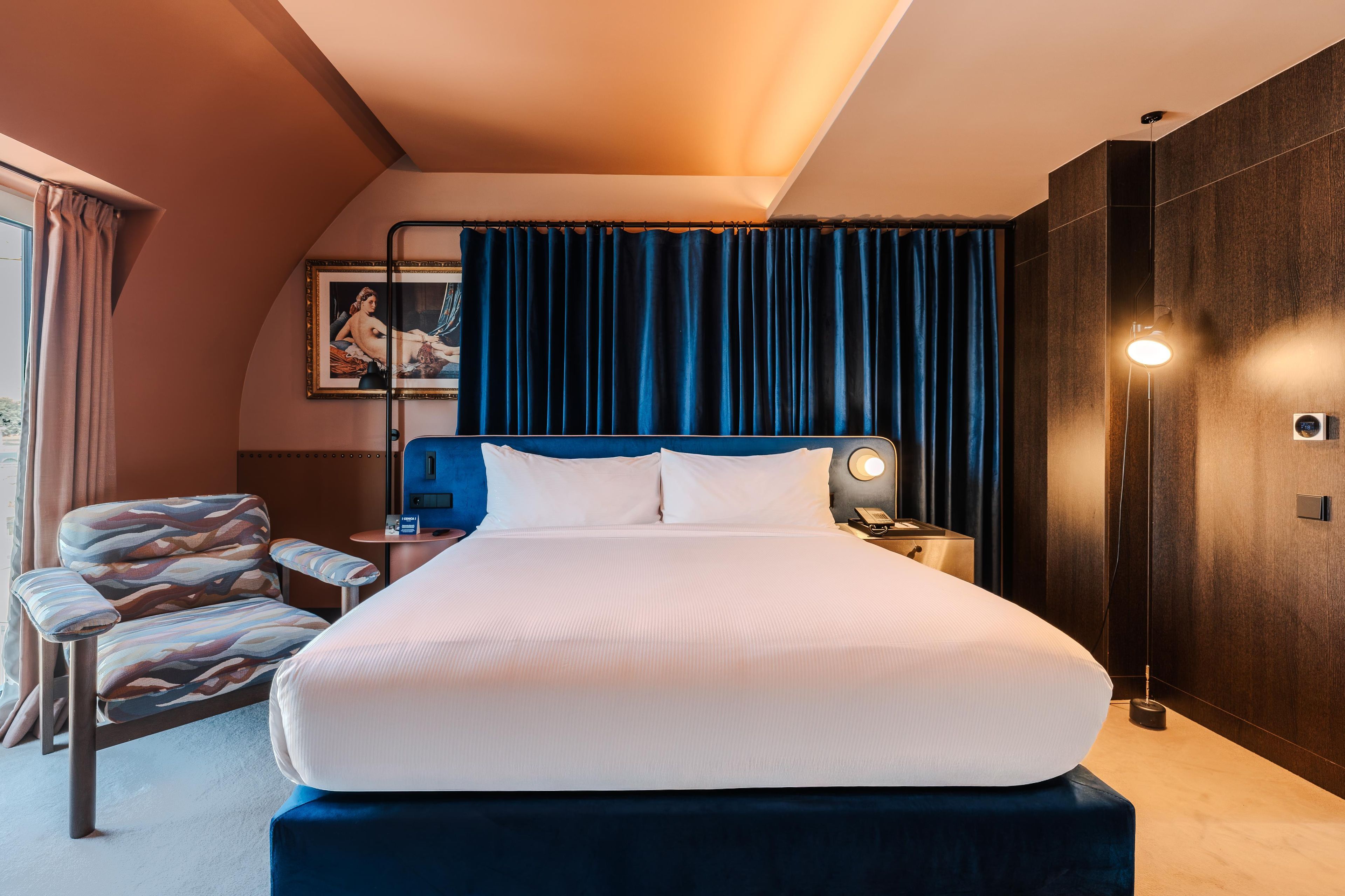 A hotel room with a large bed, a chair, a desk, and a nightstand.