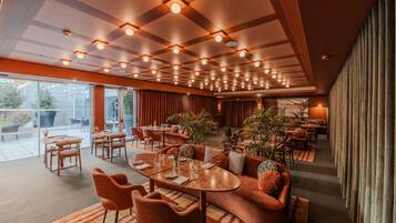 A spacious hotel lobby with multiple seating areas, a large window offering a view of the outdoors, and a modern ceiling design with recessed lighting.