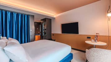 Une chambre d’hôtel avec un grand lit, une petite table, un téléviseur fixé au mur et une salle de bain visible à travers une porte ouverte.